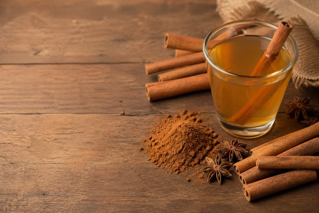 Cinnamon sticks and ground cinnamon powder with a glass of cinnamon water on a wooden surface